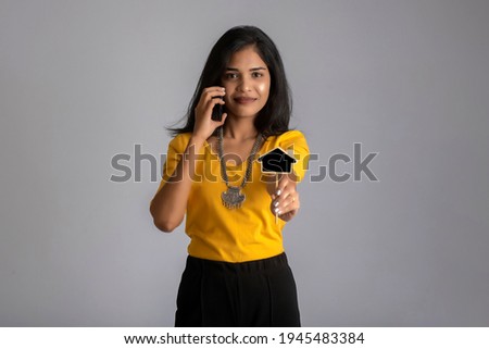 Young Indian girl using mobile phone or smartphone and showing small board on gray background.