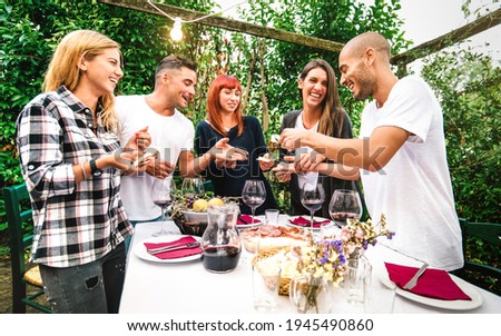 Young people having fun eating local food and drinking red wine at country side garden fest - Friendship and life style concept with happy friends together at farmhouse patio party - Warm vivid filter