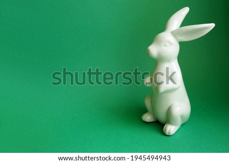 a ceramic figurine of a blue Easter bunny stands to the right on a green background side view . symbol of the Easter holiday
