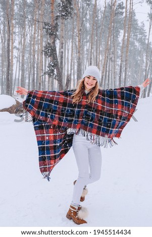 Dancing woman traveling among forest wearing hat and poncho, boho and wanderlust style. Winter is coming, first snowfall. Cold weather. Winter landscape