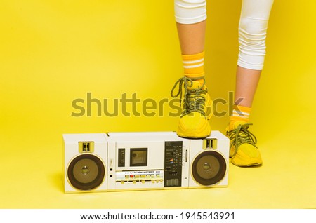 Female teenage leg in yellow sneakers stands on a retro tape recorder. Horizontal photo