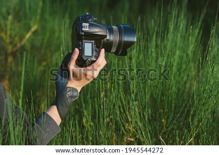 Close-up, professional photo-video camera in the hands of a girl. Against the background of green nature and forest