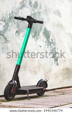 Electric scooter standing against bright wall background. E-scooter or kick scooter using with mobile app. Modern, ecological, eco-friendly urban transport. Summer in the city. Copy space, close up Royalty-Free Stock Photo #1945546774