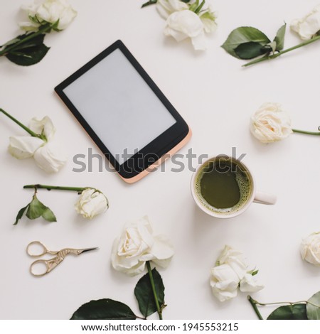 floral composition with digital tablet, white roses on white background. Minimal home office desk. Flatlay, top view. Copy space mockup template.