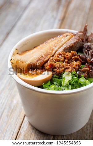A closeup view of the ingredients for a tonkatsu ramen in a to-go cup container.