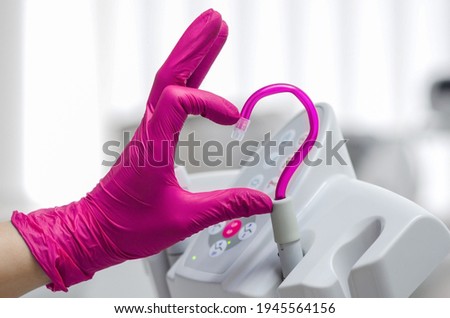 Saliva ejector and a hand in a disposable glove symbolize love in dentistry.Hand in a pink glove.Pink saliva ejector.The atmosphere of the dental office.With love in dentistry.Heart symbol. Royalty-Free Stock Photo #1945564156