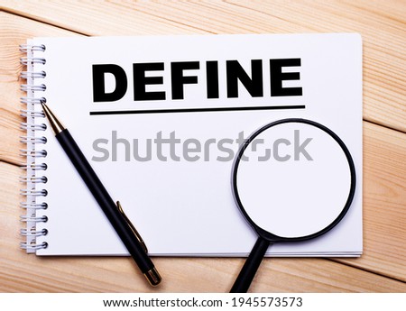 On a light wooden background lie a pen, a magnifying glass and a notebook with the text DEFINE