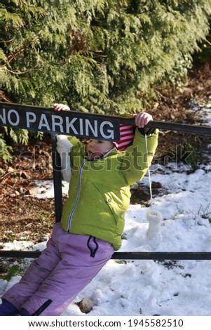 Child playing, climbing up to a no parking sign 