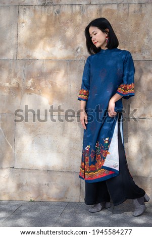 Young Vietnamese Asian model girl smiling dancing with traditional blue dress with orange and yellow details in the streets of Madrid in a natural and spontaneous way
