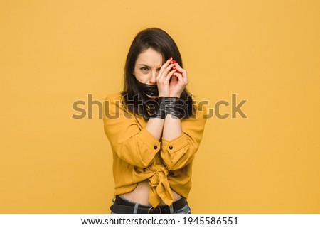 Photo of attractive female victim with her mouth taped up, kidnapping. Wears yellow shirt, isolated yellow color background.