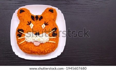 Funny salad in the form of the symbol of the tiger of 2022, made of carrots, eggs, cucumbers, potatoes, prunes, sausage. New Year's Christmas food top view copy space. Holiday, art of food