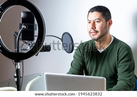 Male podcaster podcasting audio from his home studio by recording himself on his cell phone