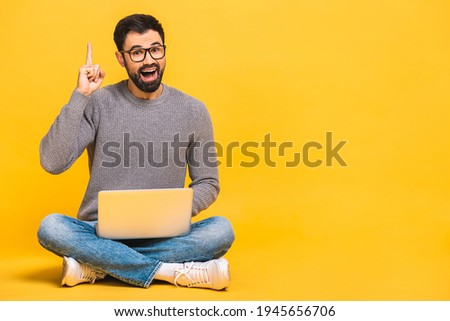Successful winner! Portrait of a happy young bearded man using laptop and celebrating success or victory isolated over yellow background.