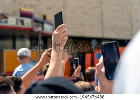 phone in hand holds over the crowd to take photos of the event. selective focusing, bright sunlight