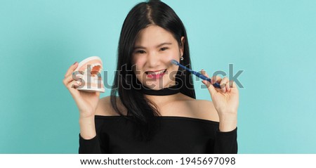 Woman holding dental teeth model or orthodontic model. Asian teenage black hair showing block of teeth for education. Pretty girl with plastic denture in hand. studio background. Oral care concept. 