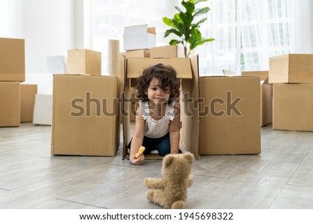 Cute toddler little baby girl playing inside cardboard boxes and eating sweet dessert while family packaging cardboard boxes for moving into a new home