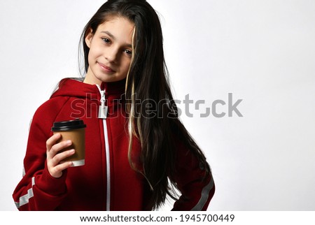 Caucasian model girl in a comfortable tracksuit drinks cappuccino coffee from a takeaway cup. Headshot studio portrait on copy space. Girls enjoy a hot flavored drink to refresh energy