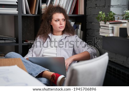 Woman sitting with laptop and looking to the window while working at her office