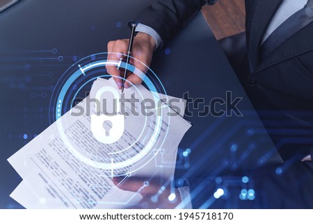 A businessman in formal wear signing the contract to prevent probability of risks in cyber security. Padlock Hologram icons over the working desk.