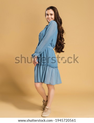 Young beautiful girl with long curly hair in a blue summer dress on a pastel orange studio background