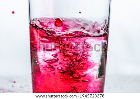 Red liquid being poured into a glass. White background.