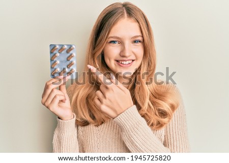 Beautiful young caucasian girl holding pills smiling happy pointing with hand and finger 