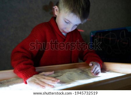 Child paint an illustration with sand on light table by