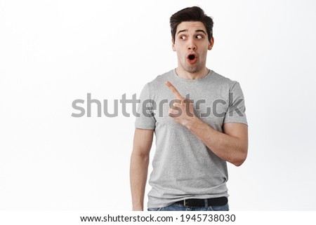 Portrait of amazed 30s guy say wow, pointing and looking left at copy space with impressed face, drop jaw from fascinating promo deal, standing over white background