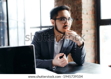 Young korean student wearing glasses sits at a table and listens attentively to others in a meeting