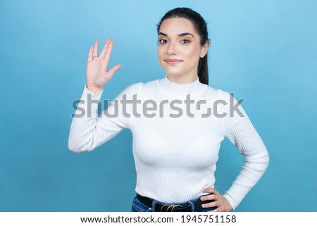 Young caucasian woman wearing white sweater over blue background doing hand symbol