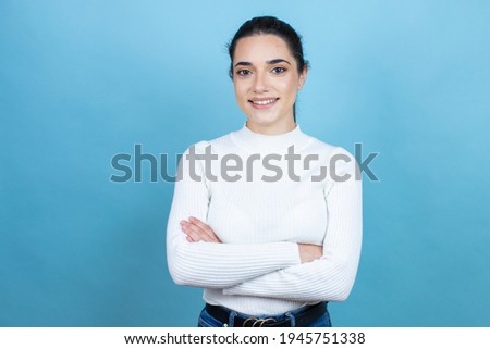 Young caucasian woman wearing white sweater over blue background with a happy face standing and smiling with a confident smile showing teeth with arms crossed