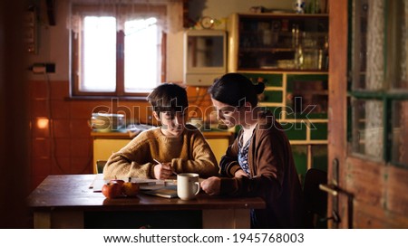 Poor mature mother and small daughter learning indoors at home, poverty concept. Royalty-Free Stock Photo #1945768003