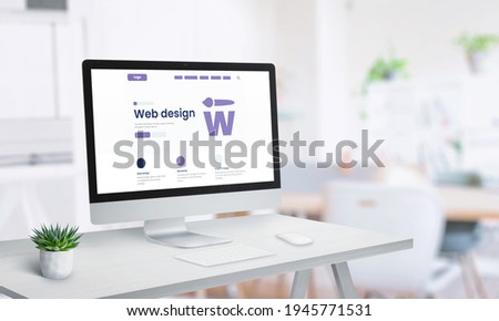 Web design studio page concept on computer display. Clean office desk with keyboard, mouse and plant Royalty-Free Stock Photo #1945771531