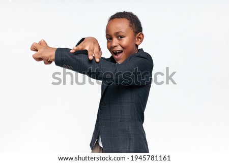 Picture of overjoyed cute African schoolboy in elegant suit opening mouth in excitement making gestures, playing, having fun. Cheerful black child enjoying leisure time after classes at school
