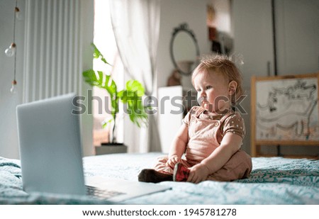 Small toddler girl on bed at home, watching story tales on laptop.