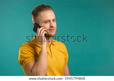 Young man speaks on phone. Guy holding and using smart phone. Yellow outfit. Blue studio background.