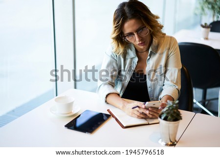 Caucaisan female blogger in optical spectacles for provide eyes correction checking received network message during time for learning in cafe interior, millennial hipster girl in glasses browsing webs