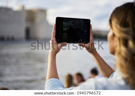 Back view of millennial female connected to roaming internet on touch pad gadget for shooting live streams vlog and photographing city landscape, tourist making pictures during travel journey