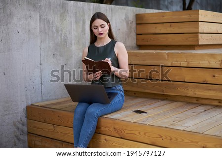 Millennial female blogger writing ideas for publication in textbook for education, skilled woman notes information in copybook using modern netbook computer during time for freelance working