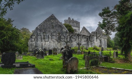 Graveyard and tombs with Celtic crosses in front of old ruins of Muckross Abbey with dramatic storm sky, Killarney National Park, Kerry, Ireland Royalty-Free Stock Photo #1945800646