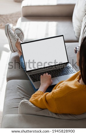 Young woman using laptop screen blank, mockup lying on the sofa at home