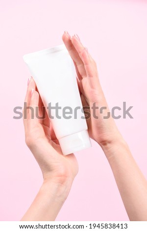 Female hand holding plastic unbranded tube on pink background. Flacon for cream, body lotion. Container for cosmetics product. Skincare and beauty concept. Mockup, copy space.conceptual shooting. Royalty-Free Stock Photo #1945838413