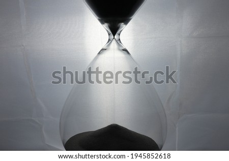 .Sand going through an hourglass with a light in the background giving it a dreamy look and black and white look to it. Photographed up close.