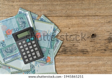Calculator and a bundle of MYR banknote on shabby wooden board background. Business concept. Copy space.