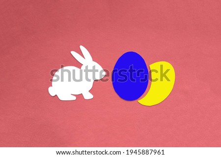The Easter bunny is white, two chicken eggs are blue and yellow on a pink background. A religious holiday. Celebration, custom.