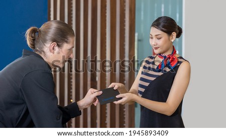 Male traveler handling passport to young female receptionist at a hotel counter for checking in. Business man showing his passport to a counter officer to identify himself for registration