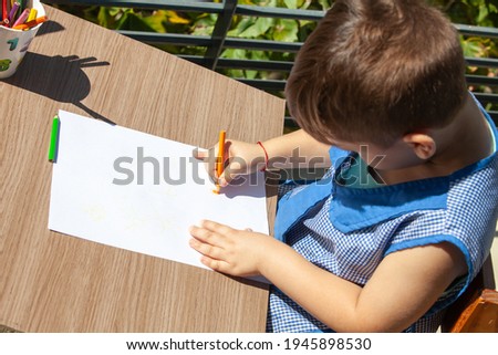little boy draws on a white sheet of paper
