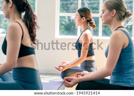 Group of Asian and Caucasian male and female sit and meditation in lotus pose before practice yoga in white studio room. Concept of diversity and healthy lifestyles