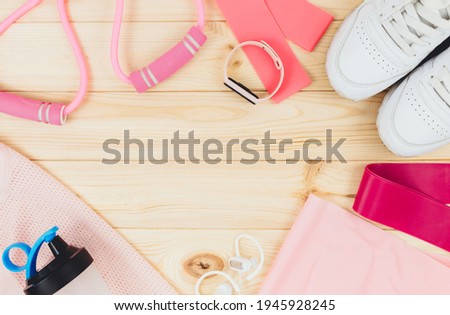 Fitness clothes and accessories for woman on wooden background. Sports fashion with t-shirt, elastic bands, headphones, sneakers, bottle. Healthy, active lifestyle concept	
