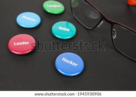 Colored plastic magnetic buttons on a black background next to glasses. Side view. Buttons with words leader, hacker, rebel, badass.